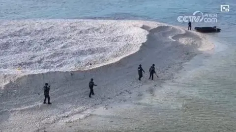 Chinese and Philippine Officials Unfurling National Flags on a Disputed Sandbar in the South China Sea